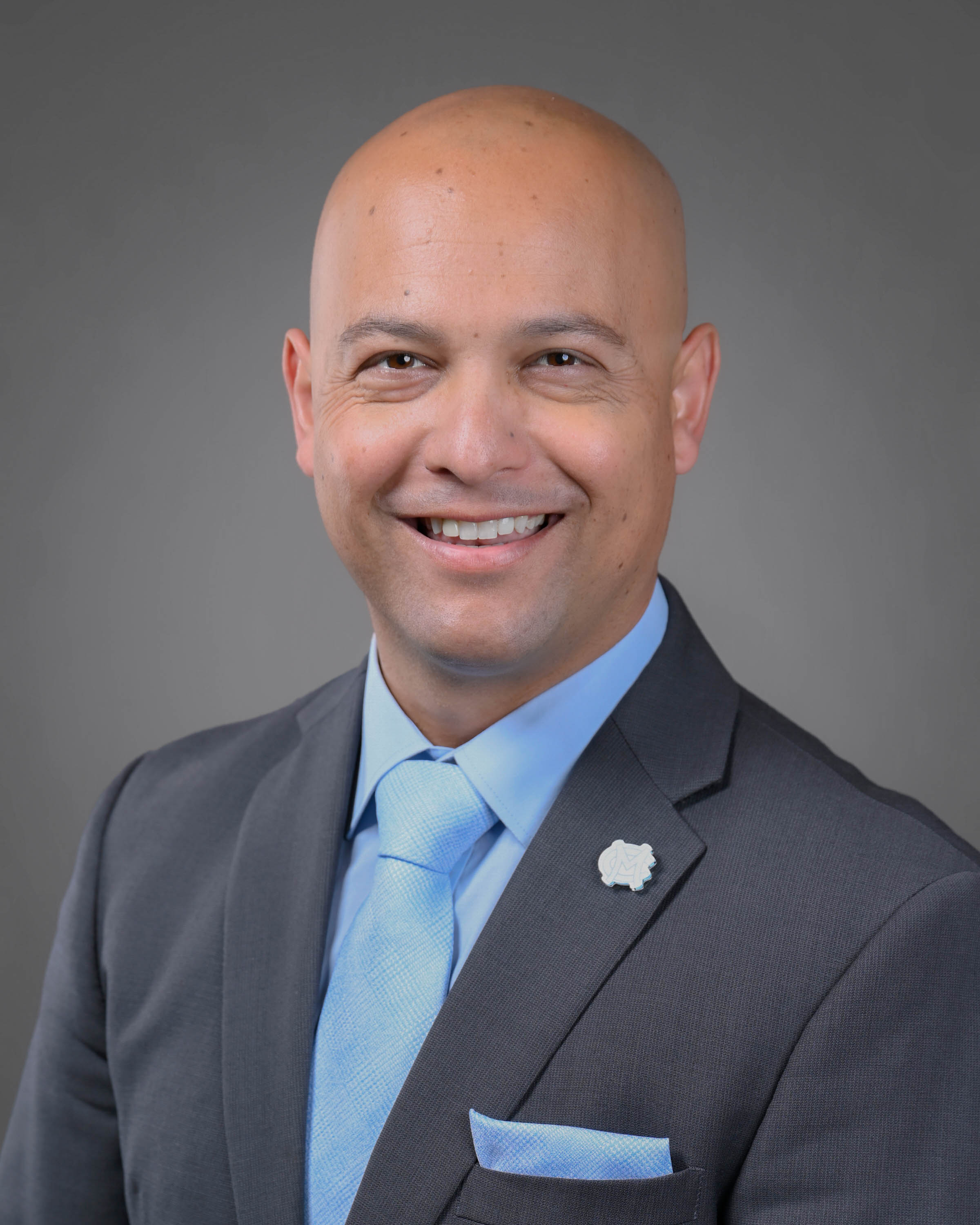 Smiling man with clean shaven head and face with a dark grey and blue suit on